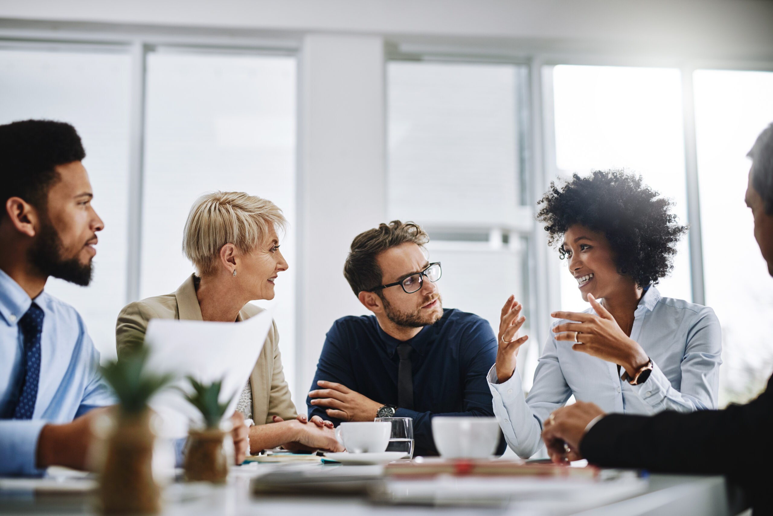 innovative technology solutions Five independent professionals in business attire sit around a table in a modern office, actively discussing strategies for handling client objections, with papers, cups, and laptops spread out before them. IT services